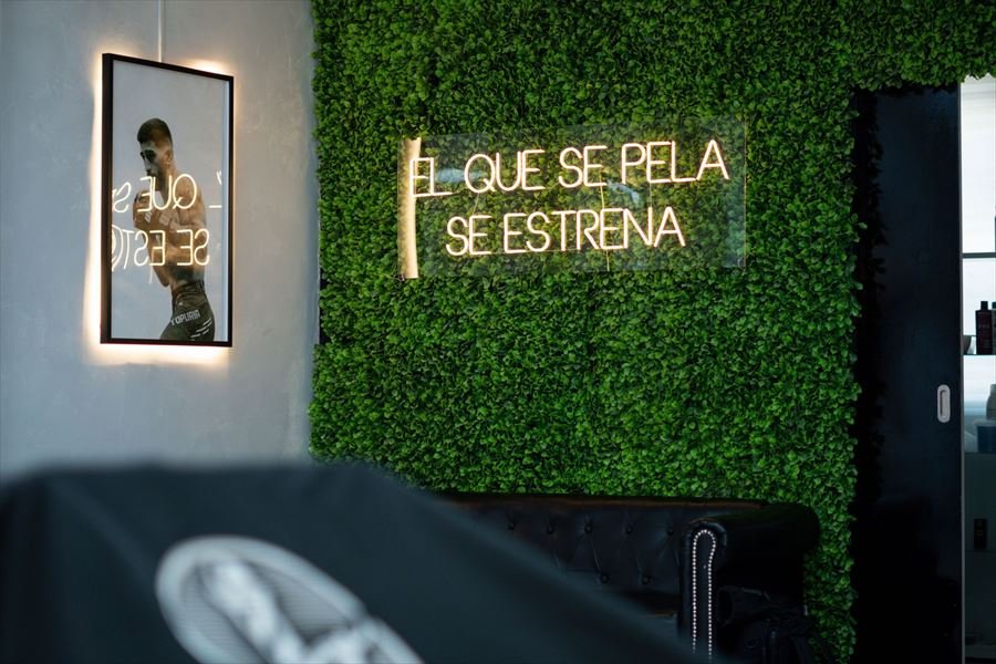 Pared vegetal con el rótulo de neón «El que se pela se estrena» en Lorenzo's Barber Studio
